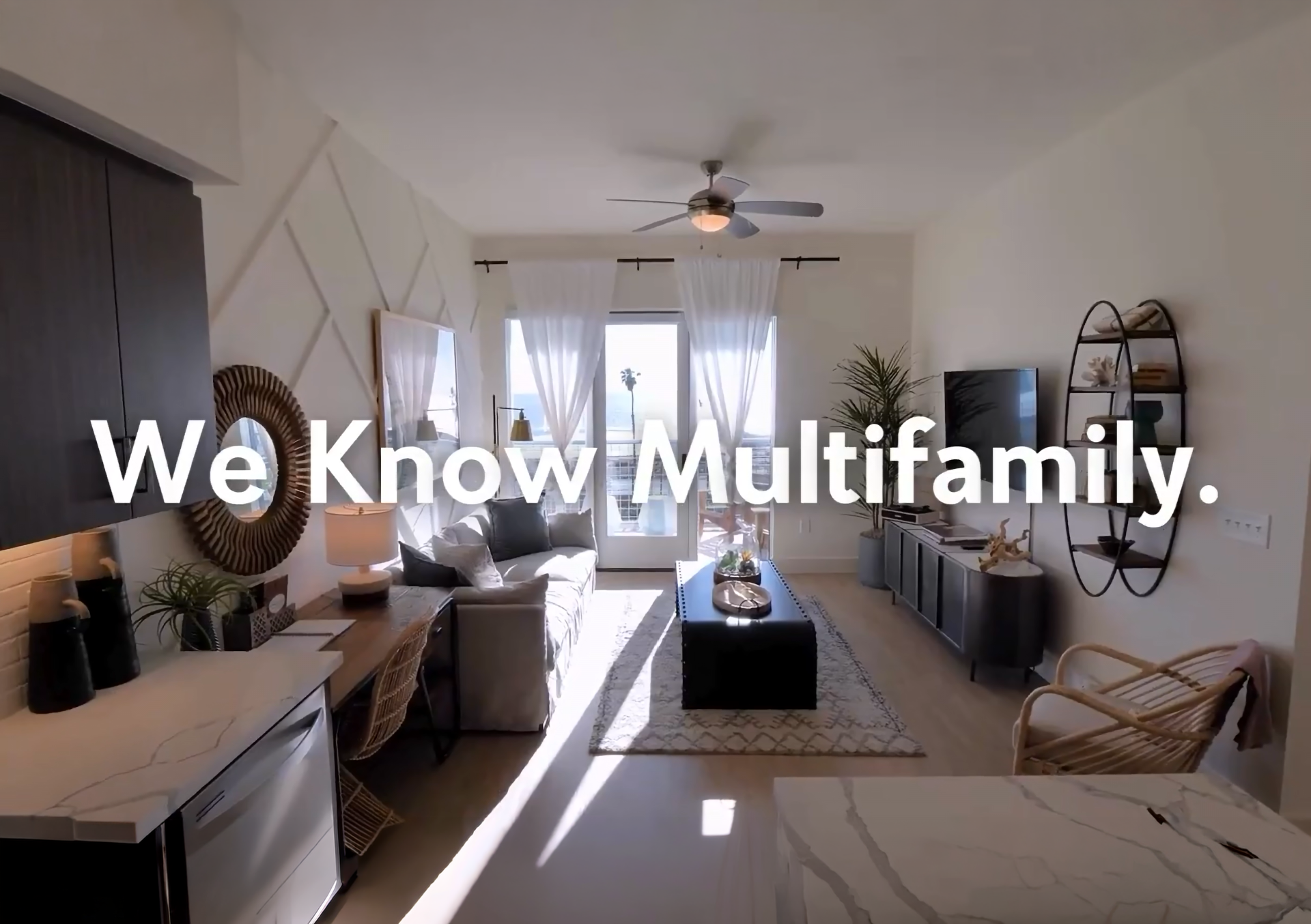 Modern living room with natural light, neutral decor, wooden furniture, a sofa, TV, and plants. Bold white text across the image reads, We Know Multifamily—a statement backed by expert multifamily marketing insights.